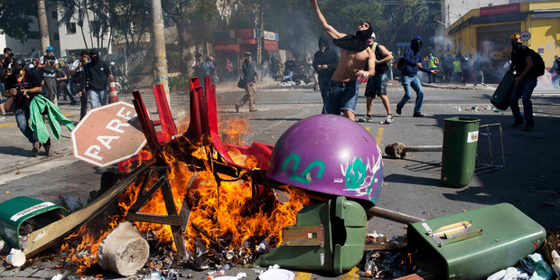 A masked man throws a stone towards riot policemen during a protest by people against the money spent on the World Cup soccer tournament, just hours before kickoff. Photo / AP