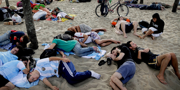 Fans sleep, rest, and rise next to a fan zone where World Cup matches are broadcast live on the Copacabana beach in the morning. Photo / AP