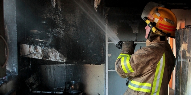 Senior firefighter Peter Harwood damps down the walls of the kitchen which was gutted by the fire. Photo/Warren Buckland