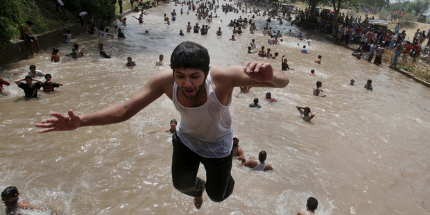 A boy jumps as people cool themselves off in a canal in Lahore, Pakistan. Photo / AP