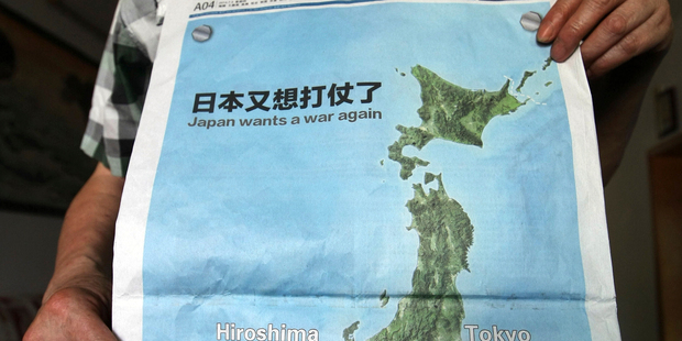 A man poses with a full page map with the headline'Japan wants a war again' and showing mushroom clouds over Hiroshima and Nagasaki. Photo / AP