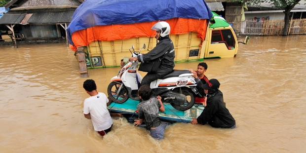 Residents help a motorist to cross a flooded street as seasonal rains and high tides cause widespread flooding. Photo / AP