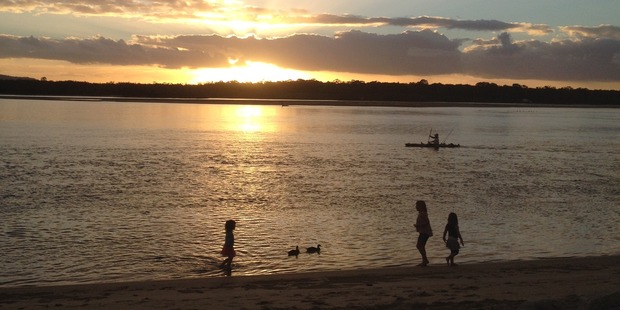 Children play on the banks of the Noosa River at Culgoa Point Beach Resort as the sun sets. Photo / Eveline Harvey