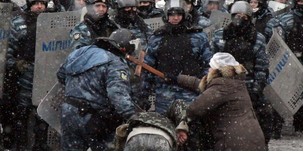 A woman hits a riot police officers with a cross as he pulls a protester during clashes in the centre of Kiev. Photo / AFP