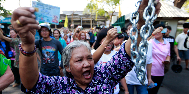 A Thai woman holds her ID card and joins with others to demand to vote outside the closed down Dindaeng district office in Bangkok on Sunday. Photo / AP