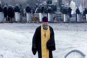 An Orthodox priest goes between riot police and opposition activists' barricades in central Kiev. Photo / AP