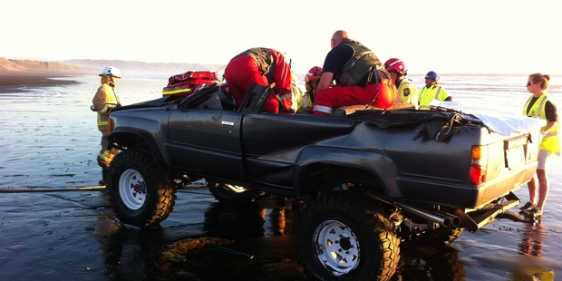 Emergency services work to free a man trapped after his 4WD rolled at Muriwai. Photo / AUCKLAND RESCUE HELICOPTER