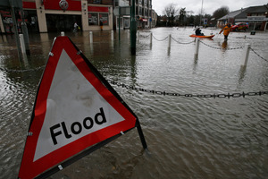 A woman sits in a boat pushed by a companion through a flooded street, in the centre of the village of Datchet, England. Photo / AP
