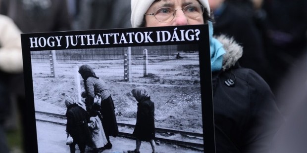 A demonstrator holds a poster of a woman with two children at a Nazi death camp with a text reading 'How were you able to go so far'. Photo / AFP
