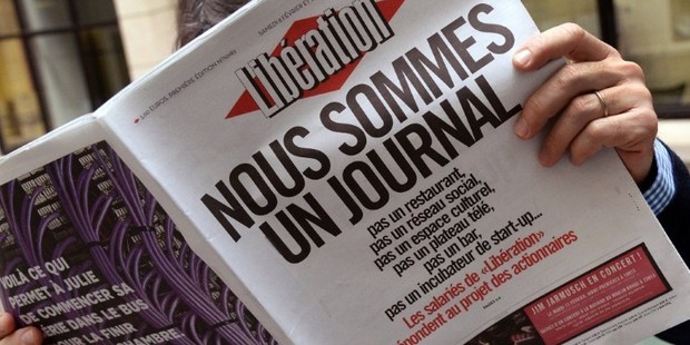 A man reads the French daily newspaper Liberation in Paris with the cover reading, 'We are a newspaper, not a restaurant, not a social network..'