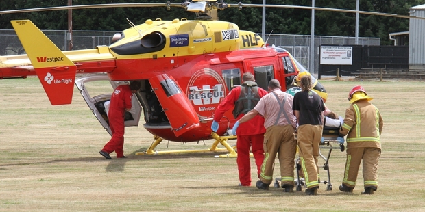 Volunteer Featherston firefighters help Life Flight Trust paramedics and flight crew load a burned man in to the waiting Westpac rescue helicopter.