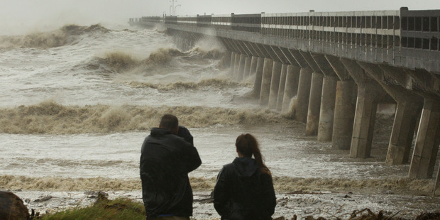 People watch as huge waves crash against the historic wharf at Tolaga Bay north of Gisborne this afternoon. Photo / Alan Gibson