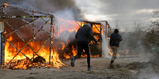 Migrants run past burning tents in a makeshift camp near Calais. Photo / AP