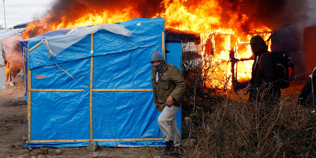 Migrants run past burning tents in a makeshift camp near Calais. Photo / AP