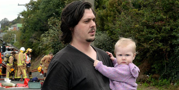 Nathan Ladbrook holds Evelyn Ladbrook (8 months) as fire engulfs their Ravensbourne Rd home yesterday. Photo / Otago Daily Times / Linda Robertson