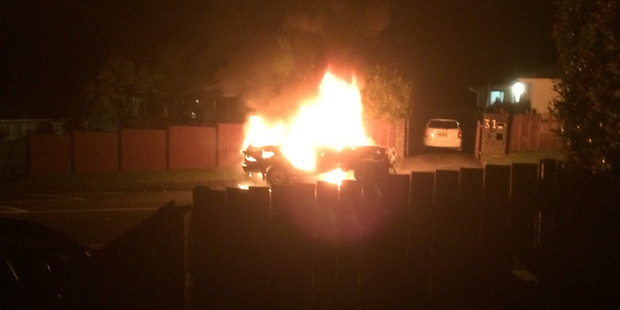 The car is well ablaze after crashing through the West Auckland fence. Photo / Julie Purcell