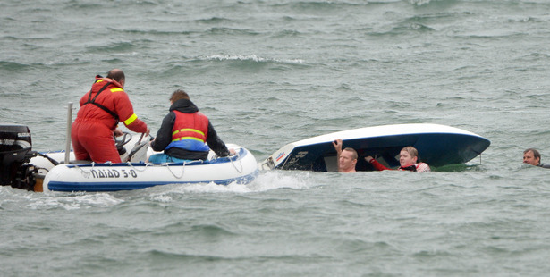 Constable Rhys Davidson (under hull on left) and Thomas George cling to a yacht while Neil George (standing in inflatable) and Maximilian Bauer (sitting) prepare to rescue them. Pic: Stephen Jaquiery