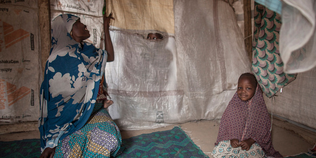 Hamsatu, 25, peeks through a tear in the divider of her tent while holding her 1-year-old daughter Hauwa on her back, as she sits next to Fatima, 3. Photo / Jane Hahn, Washington Post