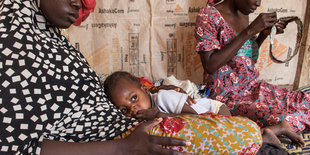 Halima, 15, holds Hauwa, 1, while Hamsatu, 25, sews a traditional prayer cap in their tent at Dalori Internally Displaced Persons Camp in Maiduguri, Nigeria. Photo / Jane Hahn, Washington Post