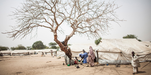 A woman feeds children who have taken shelter from the mid day sun under a bare tree at the Dalori Internally Displaced Persons Camp in Maiduguri, Nigeria. Photo / Jane Hahn, Washington Post