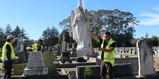 Sean Bond (left), apprentice with Headstone World, Ethan Smith, tradesman, and owner Kim Stops gently lower the angel back into place on the headstone of pioneering settlers Catrene and Boye Rosenbeck, at Mangatera Cemetery last Thursday morning. Photo / Christine McKay