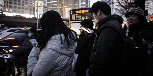 Commuters using smartphones stand in line at a bus station in Beijing in March. Market watchers agree there's a big shakeout coming. Photo / Bloomberg