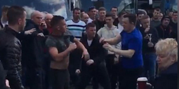 The fans trade blows as the large crowd watch on with many buses parked in the background. Photo / YouTube.