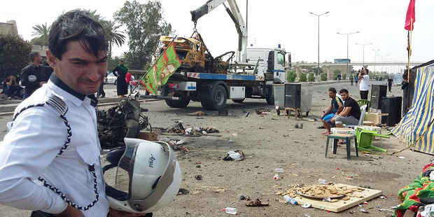 A traffic policeman grieves while security forces prepare to tow away a destroyed car after a parked car bomb went off in Baghdad's southwest. Photo / AP