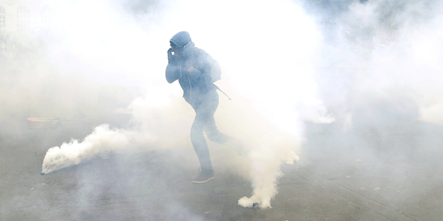 A demonstrator escapes through tear gas as he faces off with riot police officers during a protest in Paris today. Photo / AP