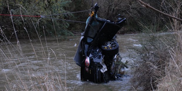 The wreckage of a late model Holden Comodore GTS is winched by heavy crane from the middle of the swollen Waipoua River.