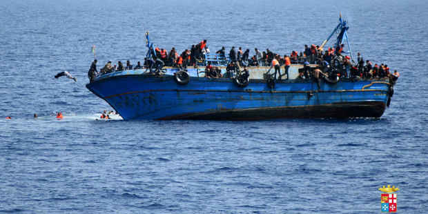 People jump out of a boat right before it overturns off the Libyan coast. Photo / Marina Militare via AP Photo
