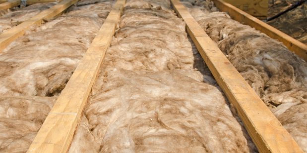 Fiber glass insulation batts unfaced between wood flooring joist cavities. Image / iStock