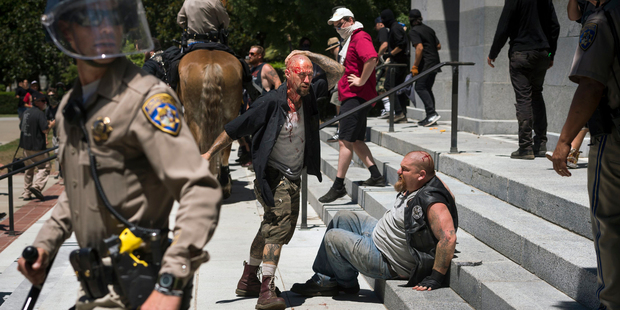 A wounded man stands by another wounded man sitting on the steps of the California state Capitol after a right-wing group clashed with counter-protesters. Photo / AP