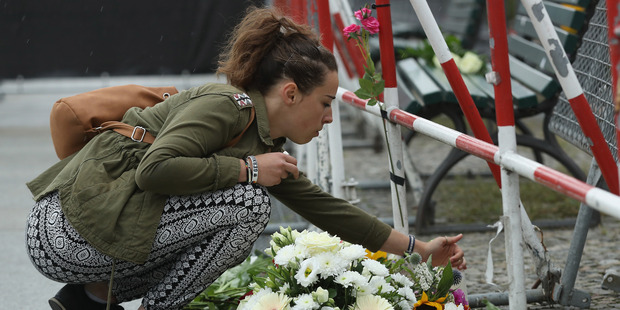 A young woman lays a candle among flowers left by mourners outside the French Embassy the day after the terror attack in Nice. Photo / Getty