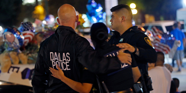 Dallas police officers comfort each other in front of police cars decorated as a public memorial Friday. Photo / AP