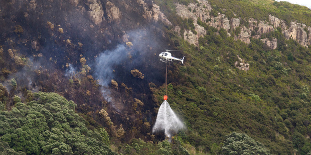 Helicopters use monsoon buckets to drop water on the remains of a bush fire that took hold near the summit of Mt Maunganui last night. Photo / Alan Gibson