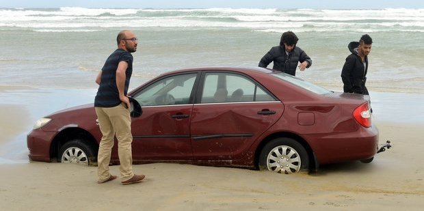 Mahmoud Helal, Ali Ibrahim and Hassan Almulla with one of their 3 cars stuck in sand on Tomahawk beach. Photo / Otago Daily Times