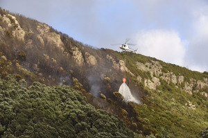 Two helicopters dump massive buckets of water on the fire on the eastern side of Mauao. Photo/George Novak