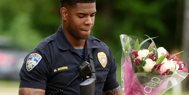 Baton Rouge Police Department Officer Markell Morris holds a bouquet of flowers and a Superman figure that a citizen left at the hospital where the officers were brought to. Photo / AP