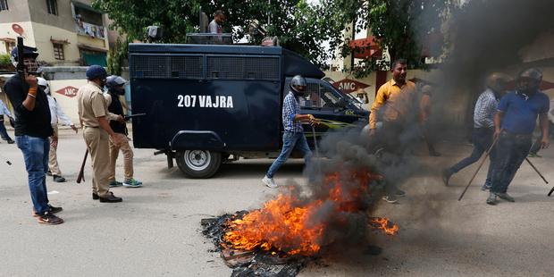 Policemen walk past flames during a protest by Dalits in Ahmadabad, India. Four men belonging to the low-caste community were beaten while trying to skin a dead cow in western India. Photo / AP