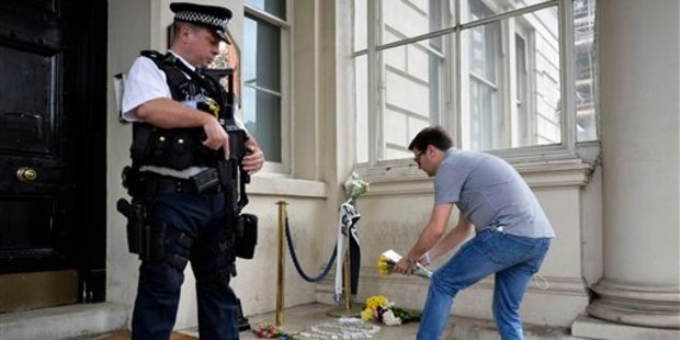 An armed police officer watches as a man lays flowers at the steps of the French Embassy in London, after a truck plowed through revelers in Nice, France. Photo / AP
