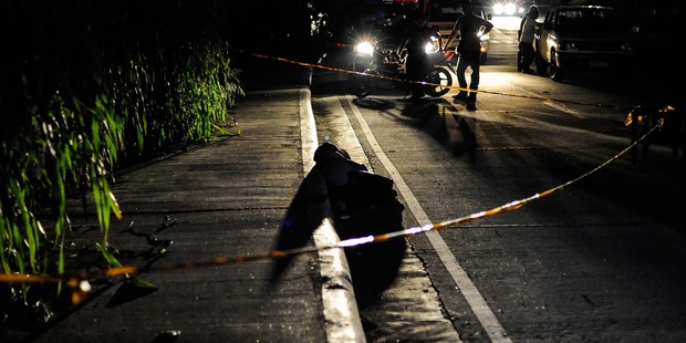 An alleged drug dealer and victim of a summary execution with his head wrapped in tape is examined by police. Photo / Getty Images