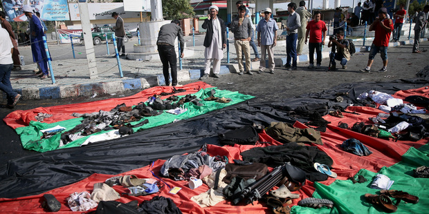 Afghans look at property left behind by victims of an explosion that struck a protest march, that is displayed on a large representation of the Afghan flag. Photo / AP