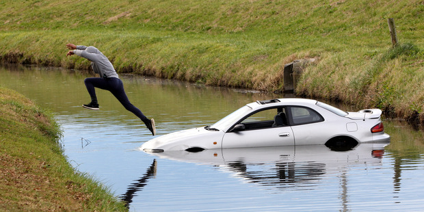 A passenger returns from a crashed vehicle after retrieving belongings through its sunroof. Photo / Paul Taylor