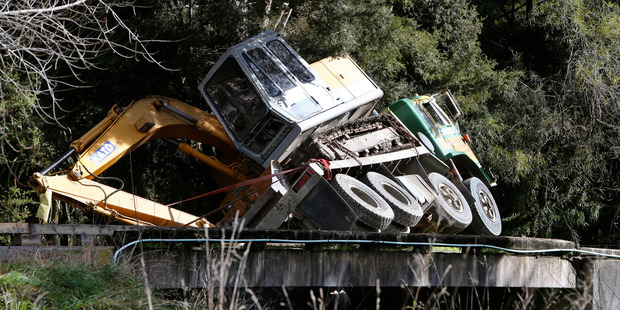 A digger is balanced precariously on the back of a truck after the bridge it was crossing gave way in Otaika yesterday morning. Photo / John Stone