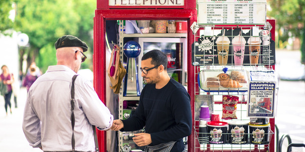 Umar Khalid, co-owner of the Kape Barako red telephone box coffee stall, serves a customer on Hampstead High Street in London. Photo / Bloomberg