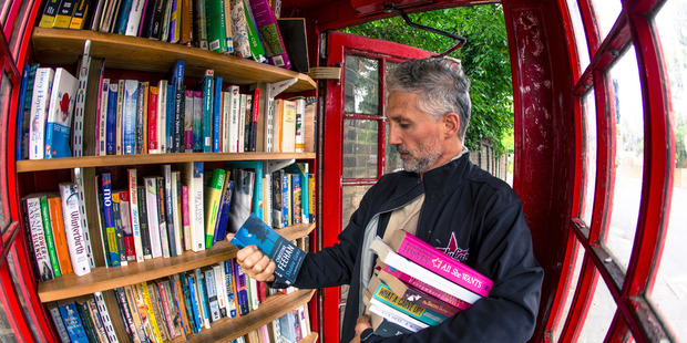 A visitor browses books in an honour library inside a converted red telephone box on Lewisham Way in London. Photo / Bloomberg