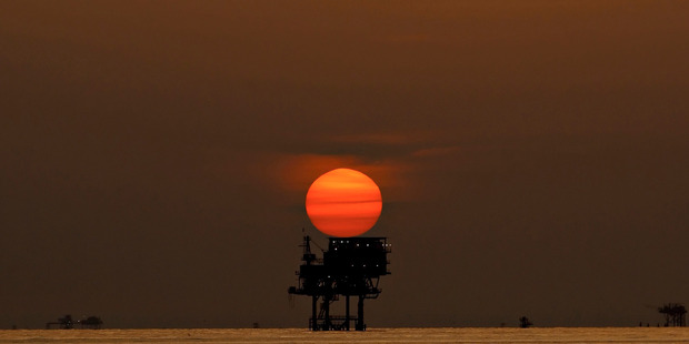 An offshore oil platform and wells are silhouetted by the setting sun in the Gulf of Mexico off the Louisiana coast. Photo / Derick E. Hingle