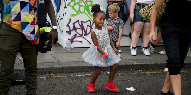 Notting Hill Carnival 2016 Children's Day. A little girl wearing a white party dress and red trainers dances in the street to a busking band. Photo / Getty