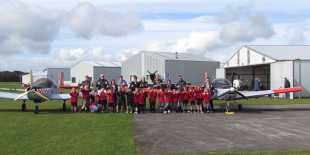 A class photo in front of the club trainer planes.